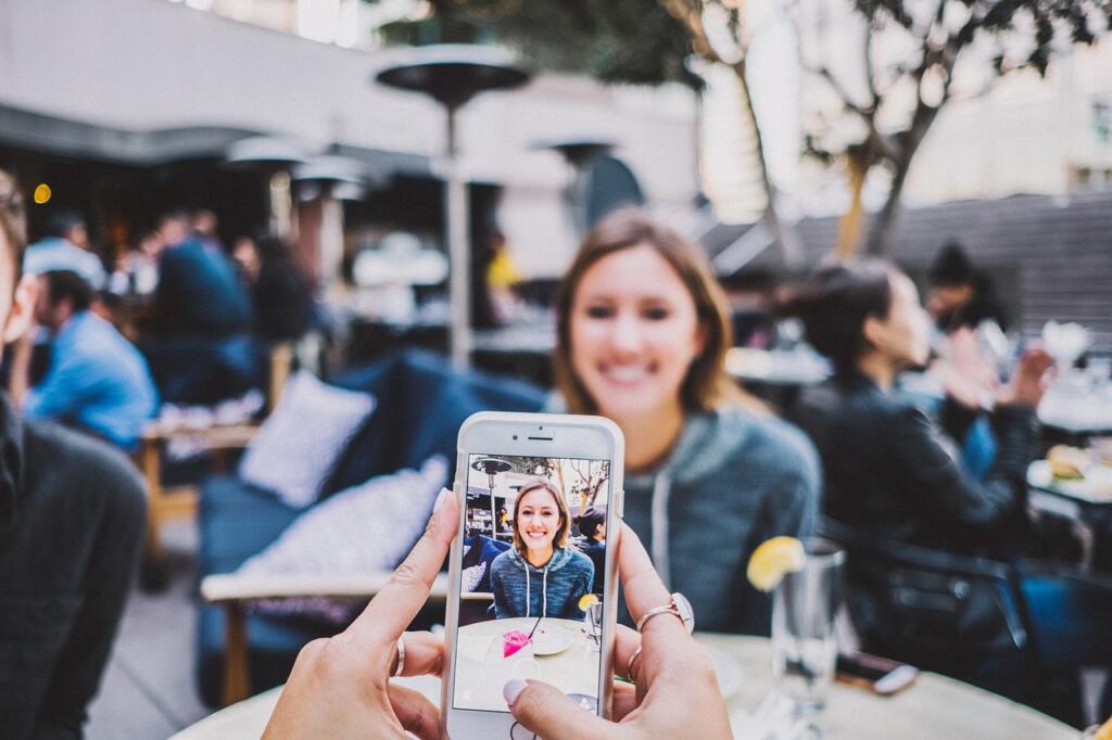 Person taking a phone photo of friends at an outdoor cafe table