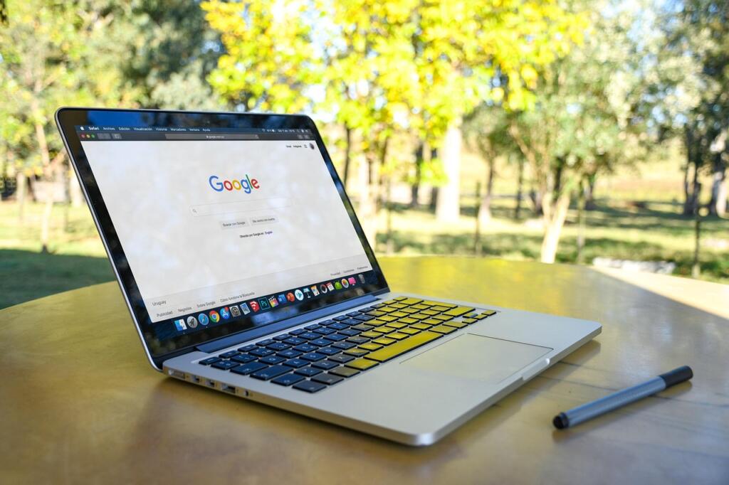Laptop open to Google search on a bench in a sunny park