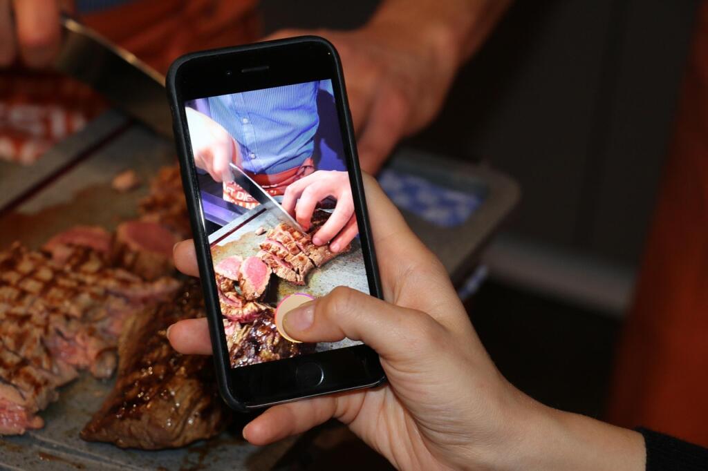 Hand photographing a plated steak dinner with a phone